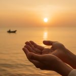 Mãos abertas recebendo luz dourada sobre o oceano ao amanhecer, simbolizando abundância espiritual e fé.