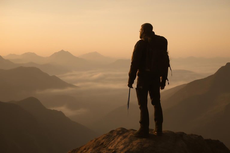 Alpinista no topo de uma montanha ao amanhecer, simbolizando a pressão e o peso do legado após a vitória.