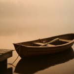Barco a remo ancorado em doca com neblina ao amanhecer, representando persistência diante do medo